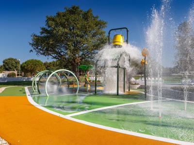 Bunter Wasserspielplatz im Freien mit Spritzdüsen, Fontänen und einem großen Wasserhut.