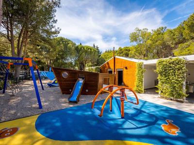 Bunter Kinderspielplatz mit Rutsche, Klettergeräten und Schiff in einem Hotelgarten unter blauem Himmel.
