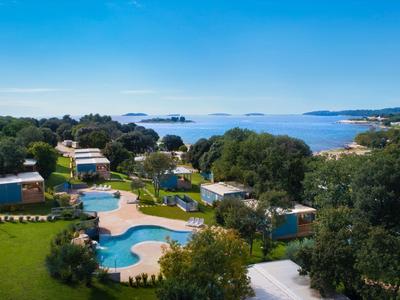 Blick auf ein Hotelgelände mit Pools, Bäumen und Blick auf das Meer unter klarem Himmel.