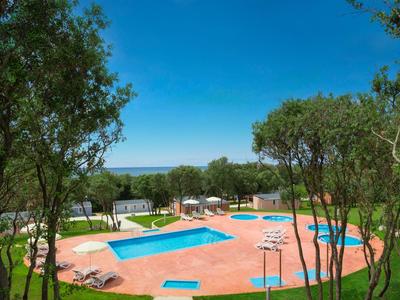 Freizeitbereich mit zwei Pools, Sonnenliegen und Bäumen unter klarem blauem Himmel.