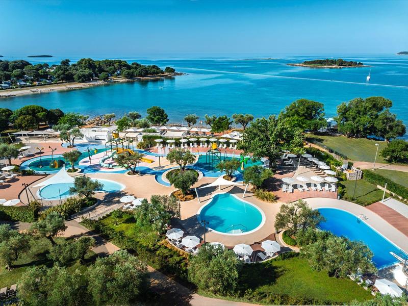 Uitzicht op een groot resort met meerdere zwembaden, ligstoelen en directe toegang tot zee.