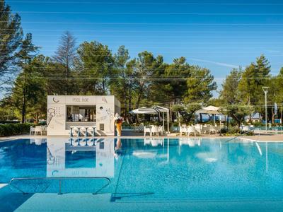 Duży basen na świeżym powietrzu z białymi leżakami obok domku przy basenie i drzewami w tle