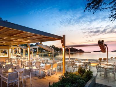 Strandrestaurant mit weißen Stühlen und Tischen bei Sonnenuntergang und Blick auf das Meer.
