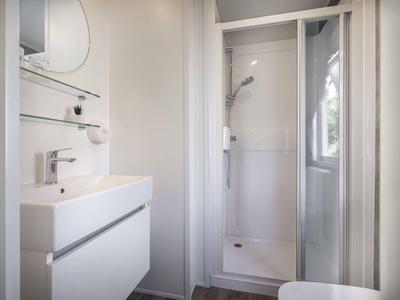 Baño pequeño y moderno con lavabo blanco, espejo y ducha con mampara.