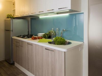 Cocina moderna con frentes de madera, área de trabajo clara y respaldo de vidrio en una habitación de hotel.