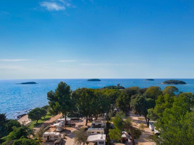 Vista de una línea costera con árboles y áreas de camping bajo un cielo azul despejado.