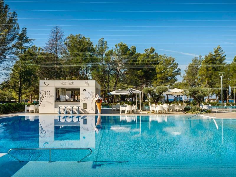 Una piscina exterior tranquila con tumbonas y árboles al fondo en un día soleado.