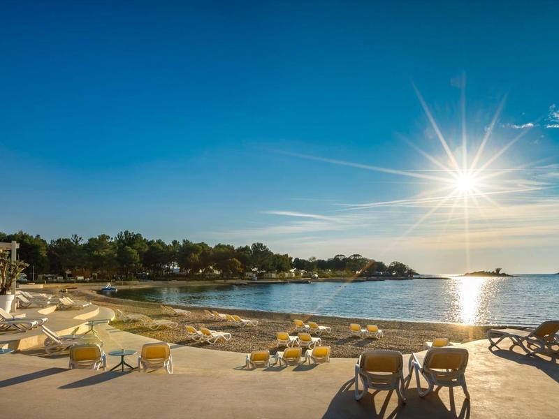 Playa soleada con tumbonas y mar tranquilo bajo un cielo claro al atardecer.