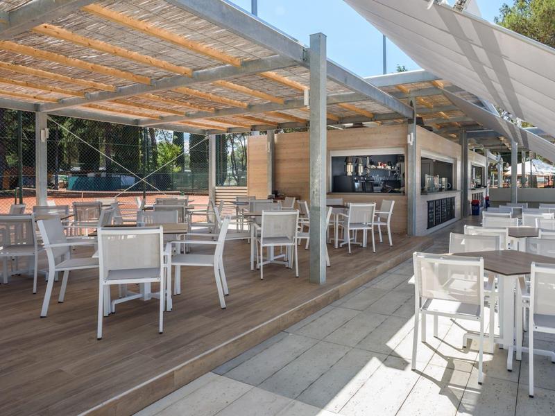 Restaurante al aire libre con mesas y sillas blancas bajo sombra en un hotel.