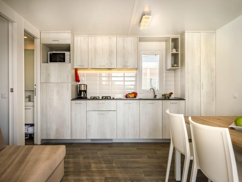 Pequeña cocina moderna en espacio luminoso con armarios blancos y área de comedor.