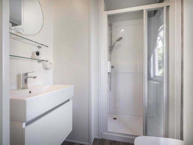 Baño pequeño y moderno con lavabo blanco, espejo y ducha con mampara.