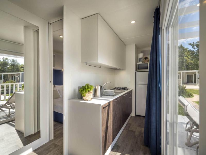 Cocina moderna con armarios blancos y madera clara junto a una terraza con jardín soleado