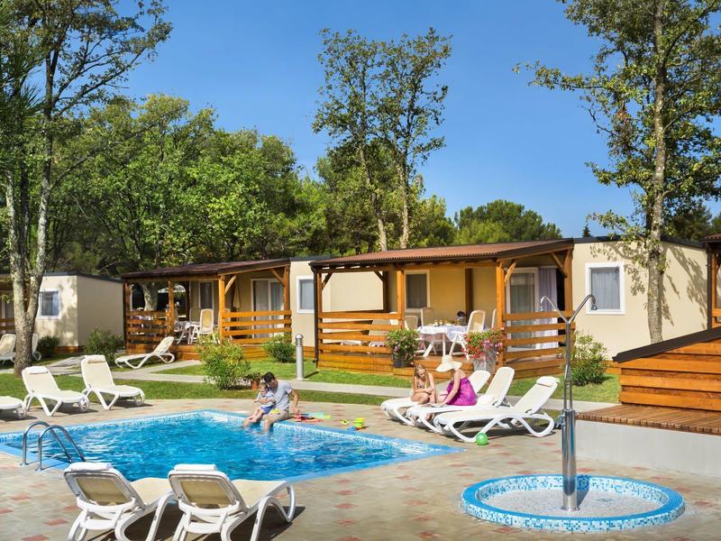 Complejo de casas de vacaciones acogedoras con piscina y tumbonas en un entorno verde.