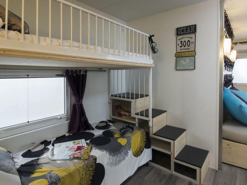 Nicho de descanso acogedor con litera y ventana, al lado una escalera y zona de asientos con cojines azules.