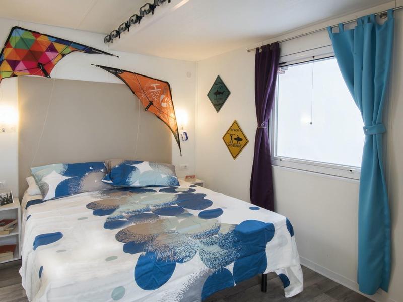 Acogedor dormitorio con cama colorida y ventana con cortinas azules y moradas.