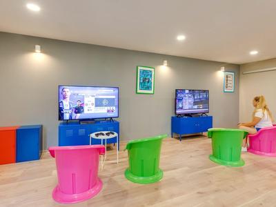 Moderne speel- en loungekamer met kleurrijke stoelen en aan de muur gemonteerde tv's.