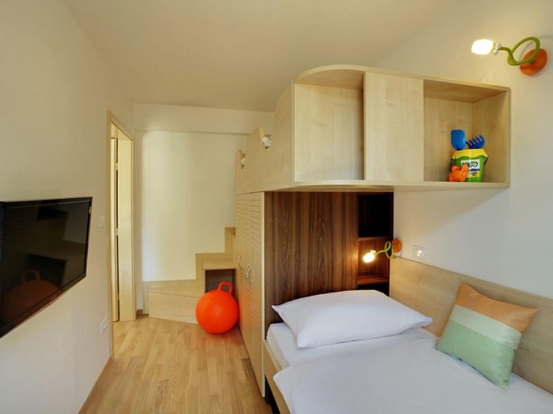 Compact hotelkamer met eenpersoonsbed, wand-tv en ingebouwde planken, minimalistisch ontwerp.