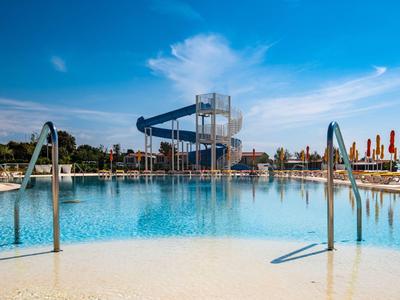 Grande piscina con scivolo d'acqua e ombrelloni sotto un cielo blu.