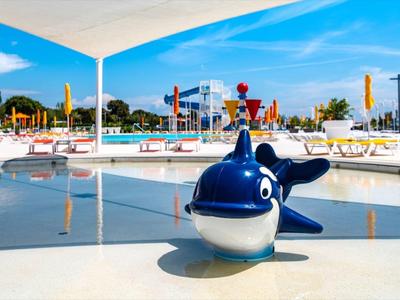 Bazén s modrou velrybí fontánou v popředí a lehátky v pozadí.