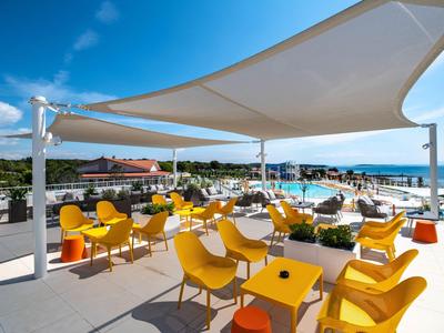 Terrazza sul tetto con sedie gialle, tavoli e tende da sole con vista sul mare e sul cielo.
