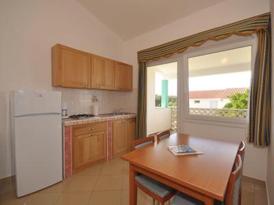 Malý kuchyňský kout s dřevěnými skříňkami, lednicí, stolem a židlemi u otevřeného okna.