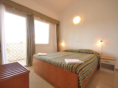 Světý hotelový pokoj s manželskou postelí, balkonem a jednoduchým dřevěným nábytkem.