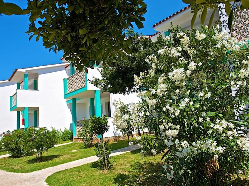 Moderní bílá budova se zelenými akcenty a kvetoucími keři pod jasnou oblohou