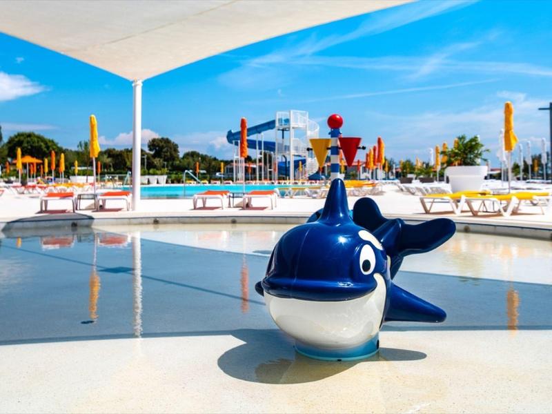 Bazén s modrou velrybí fontánou v popředí a lehátky v pozadí.