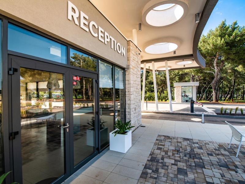 Vnější pohled na vchod do hotelu s recepcí a zastřešenou chodbou za denního světla
