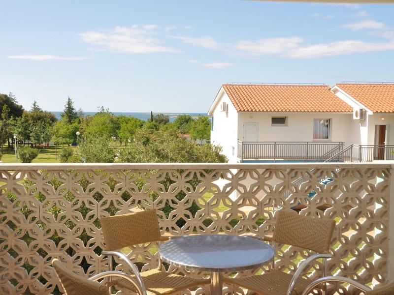 Balkon s malým kulatým stolem a dvěma židlemi, výhled na domy a zelenou krajinu.