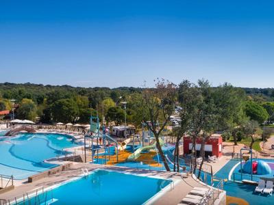 Grande piscina dell'hotel con parco acquatico e alberi circostanti sotto un cielo sereno.