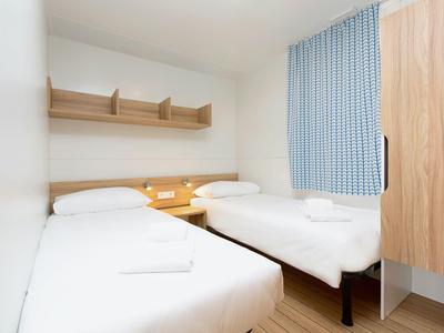 Una habitación de hotel luminosa con dos camas individuales, muebles de madera y cortinas azules.
