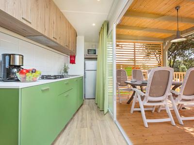 Cucina moderna con mobili verdi che si apre su terrazza coperta con area pranzo.