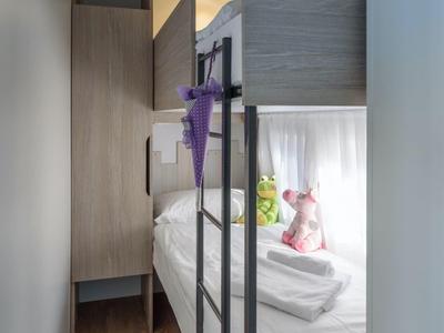 Stanza stretta con letto a castello, biancheria e peluche vicino alla finestra.