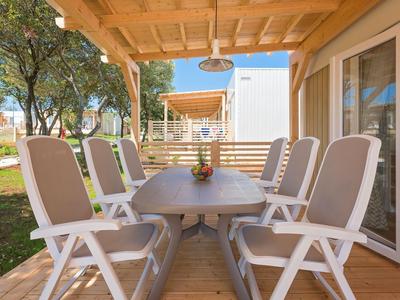 Patio cubierto con gran mesa de comedor y seis sillas cómodas en una casa de vacaciones.