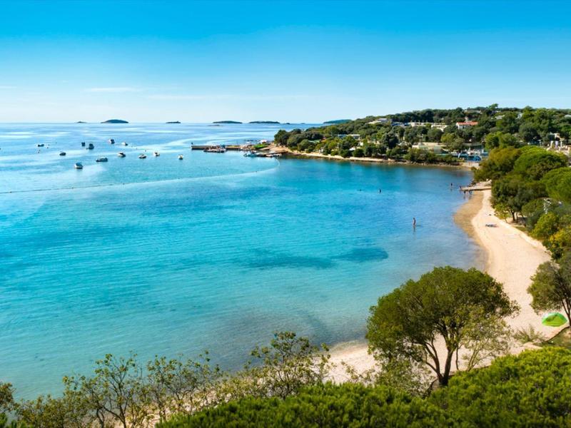 Spiaggia blu chiara con alberi e barche all'orizzonte sotto il sole.