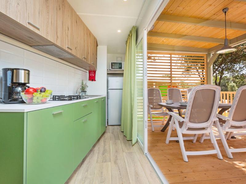 Cucina moderna con mobili verdi che si apre su terrazza coperta con area pranzo.