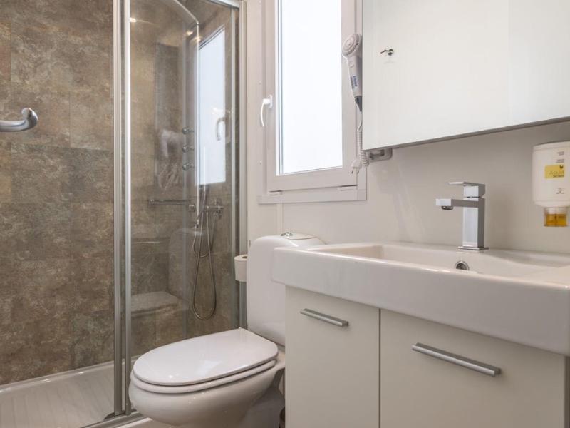 Bagno moderno con doccia, WC e mobile bianco sotto la finestra.