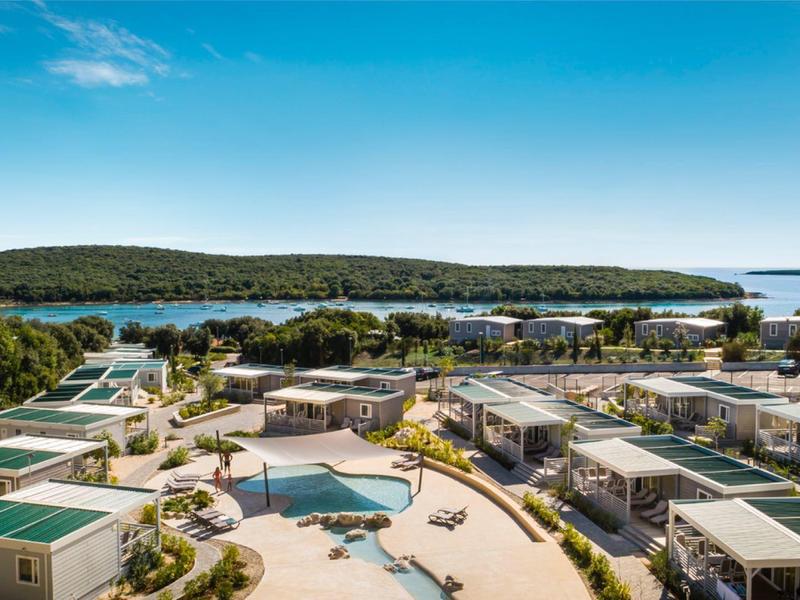 Vista di un resort con piscina, bungalow e ambiente verde sotto un cielo azzurro.