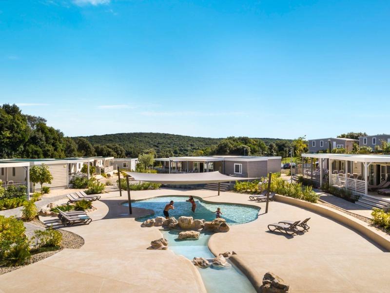 Complesso alberghiero moderno con piscina, circondato dalla natura e da un cielo azzurro limpido.