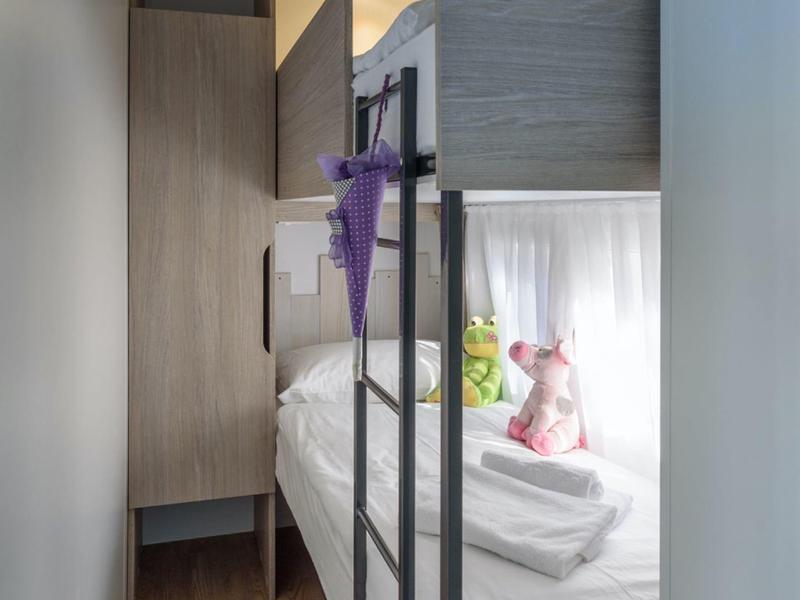 Stanza stretta con letto a castello, biancheria e peluche vicino alla finestra.