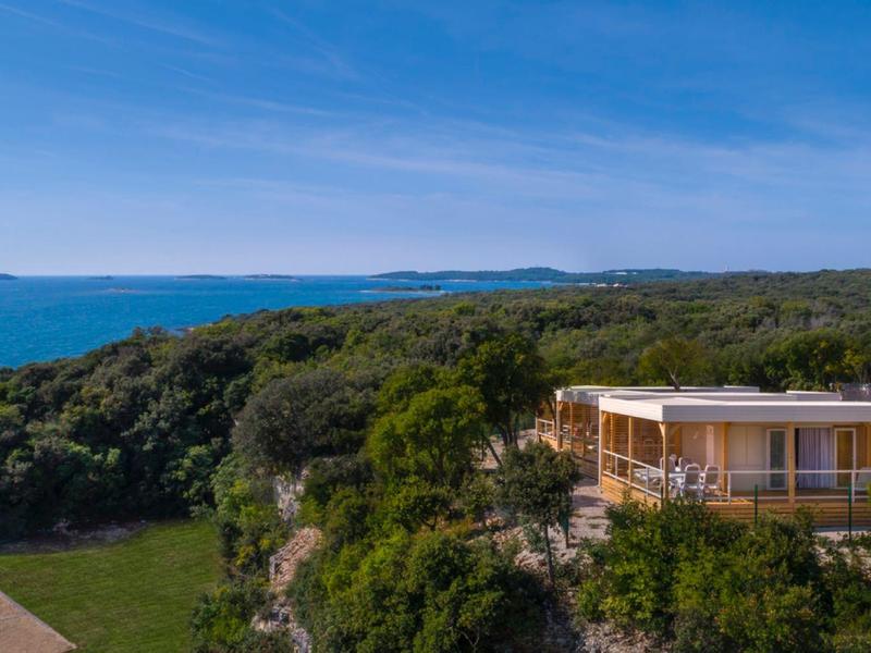 Casa moderna su scogliera con vista mare e foresta sullo sfondo sotto un cielo limpido.