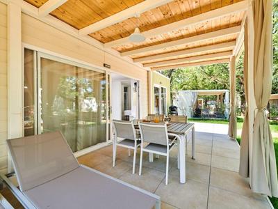 Patio cubierto con mesa de comedor, sillas y tumbona junto a una ventana de la casa.