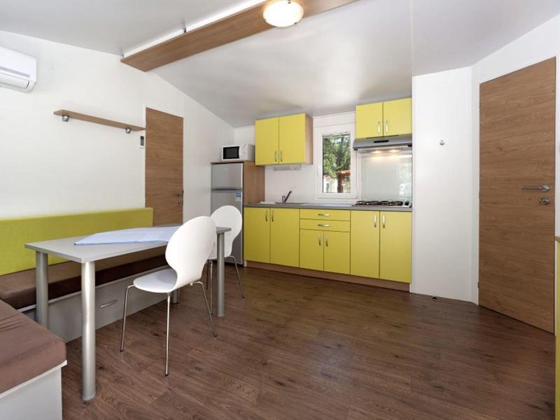 Moderner Küchenraum mit gelben Schränken, Holzboden, weißen Stühlen und grünem Sitzbereich.