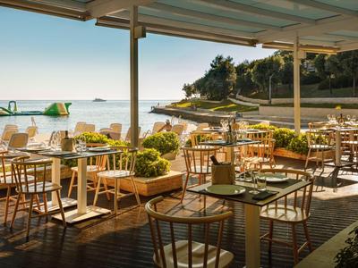 Restaurant en plein air avec tables et chaises sur une véranda avec vue sur la mer sous le soleil.