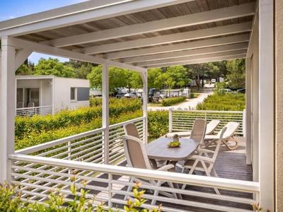 Terrasse couverte avec table et chaises, entourée de verdure et de bâtiments.