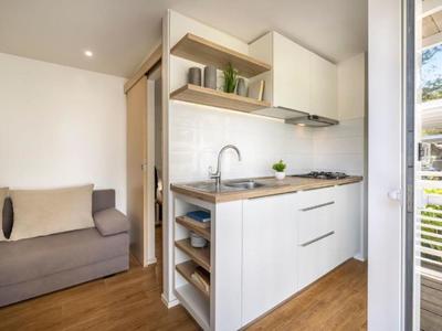 Petite cuisine moderne avec armoires blanches et plan de travail en bois à côté d'un canapé gris.