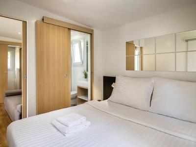 Chambre lumineuse avec lit blanc, serviettes et porte coulissante vers une autre pièce.