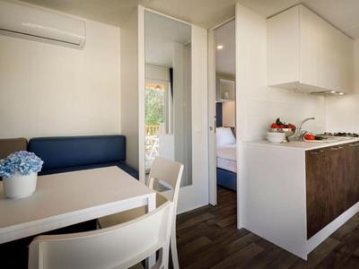 Appartement de vacances lumineux avec coin cuisine, table à manger et banc bleu.