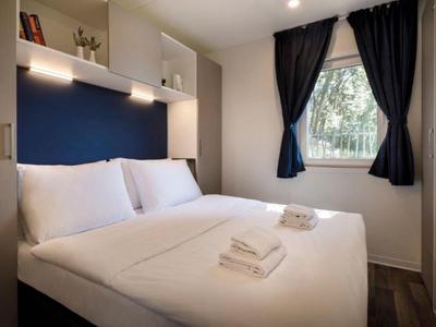 Chambre d'hôtel moderne avec un grand lit double, une literie blanche et une fenêtre avec des rideaux foncés.